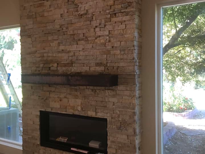 Floor-to-ceiling travertine stacked stone fireplace with linear insert by Warrens Masonry