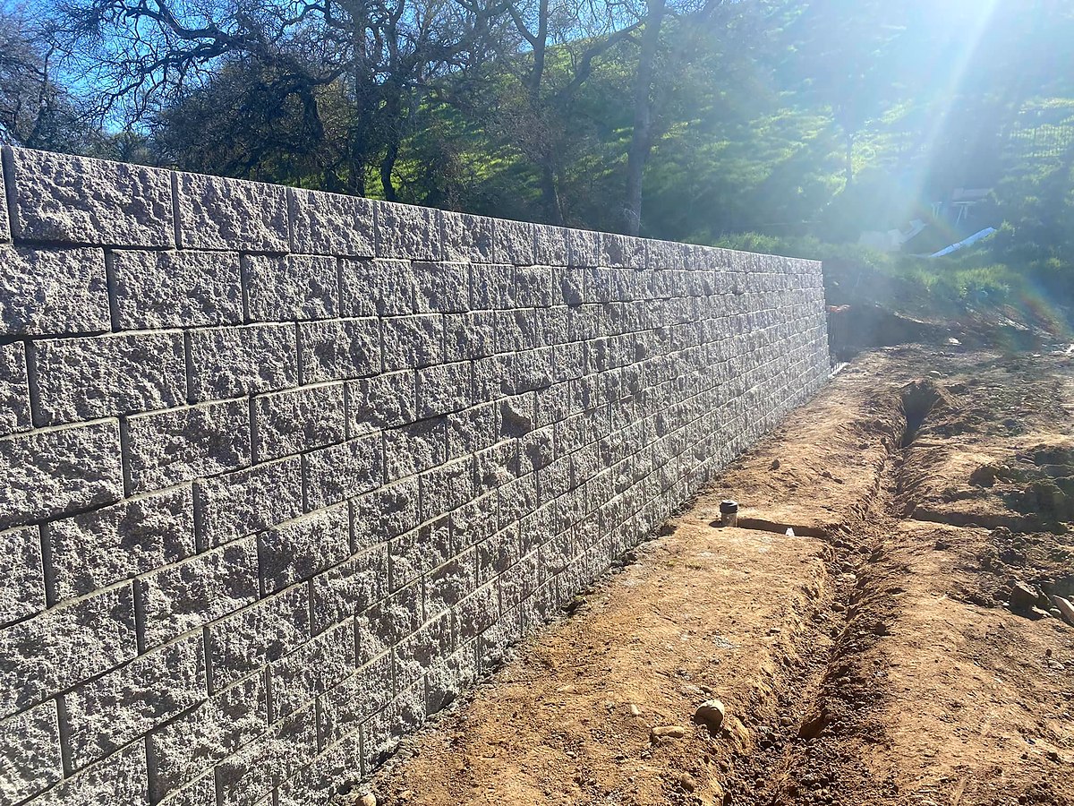 Long segmental concrete block retaining wall on hillside by Warrens Masonry