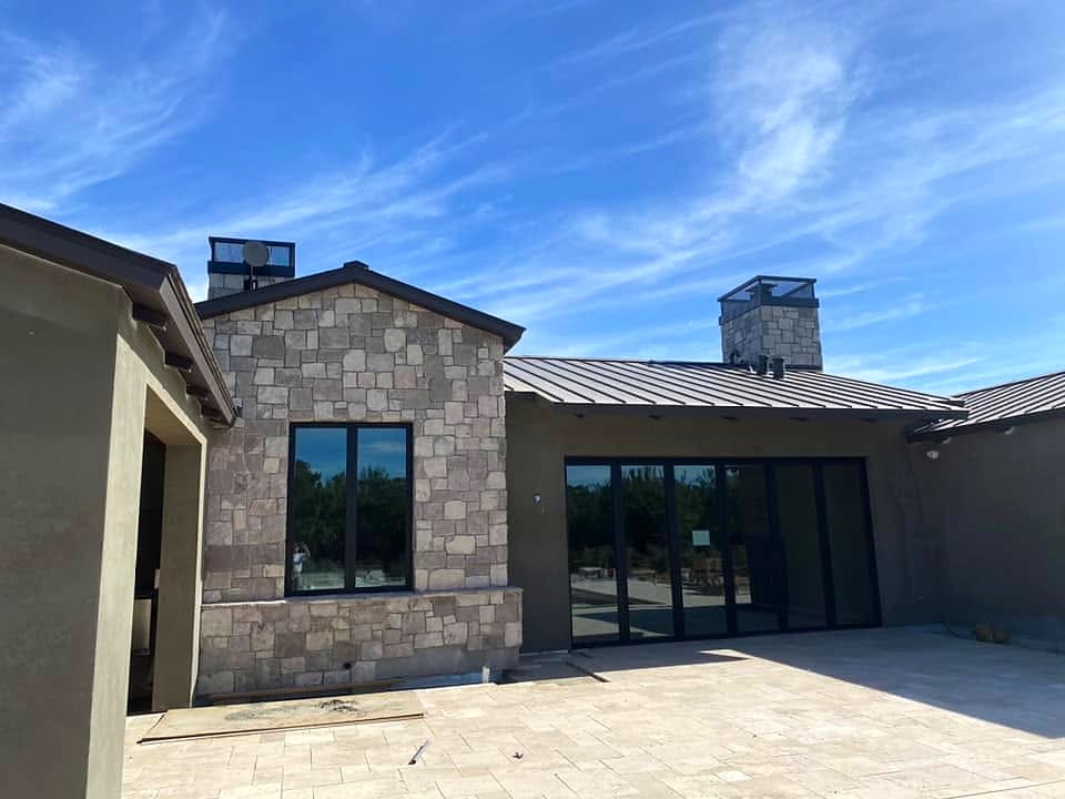 Full stone veneer home exterior with dual chimneys and travertine patio by Warrens Masonry